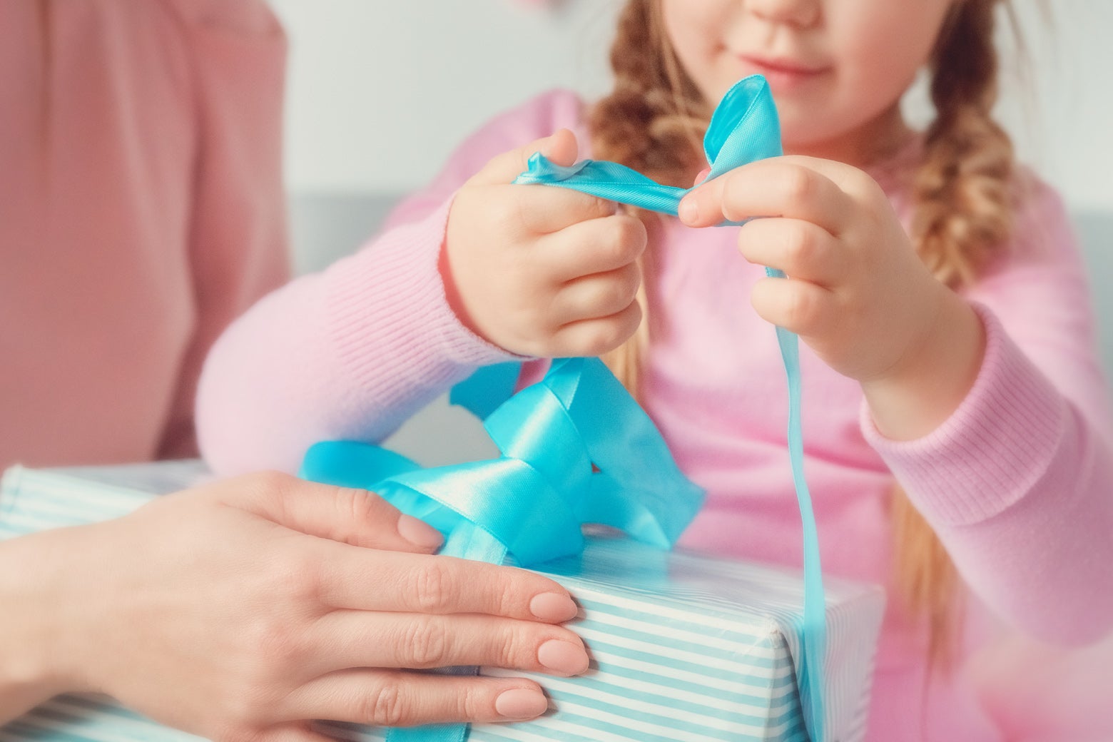 A child untangles blue ribbon from a wrapped present.