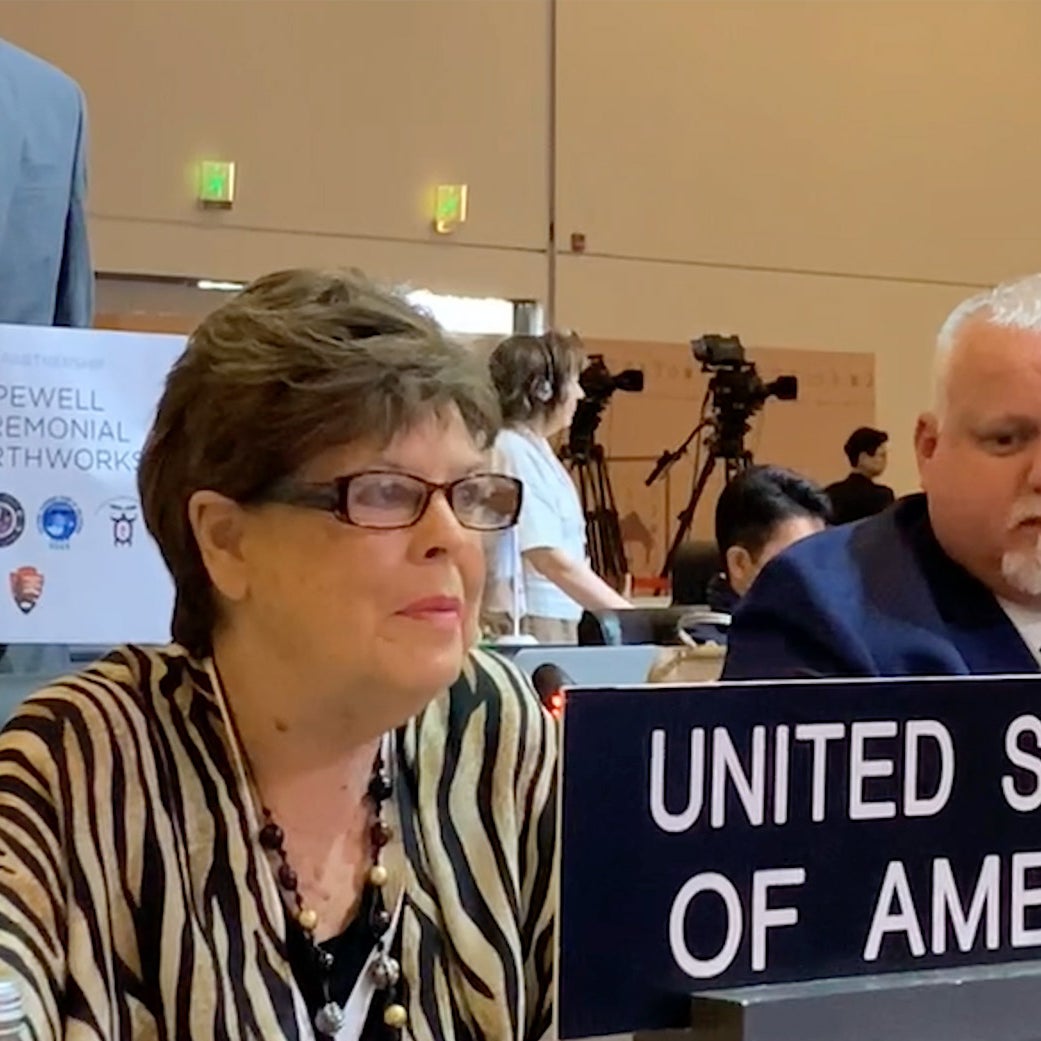 Chief Glenna Wallace sits behind a sign reading "United States of America " at the UNESCO World Heritage Site Committee meeting. 
